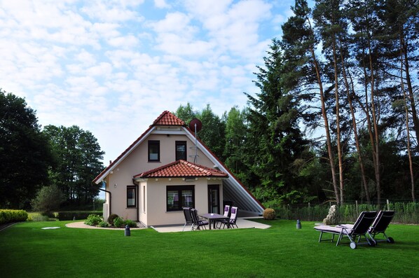 Ein Haus mit geneigtem Dach, einer Terrasse mit Sitzgelegenheiten und einem Rasen.