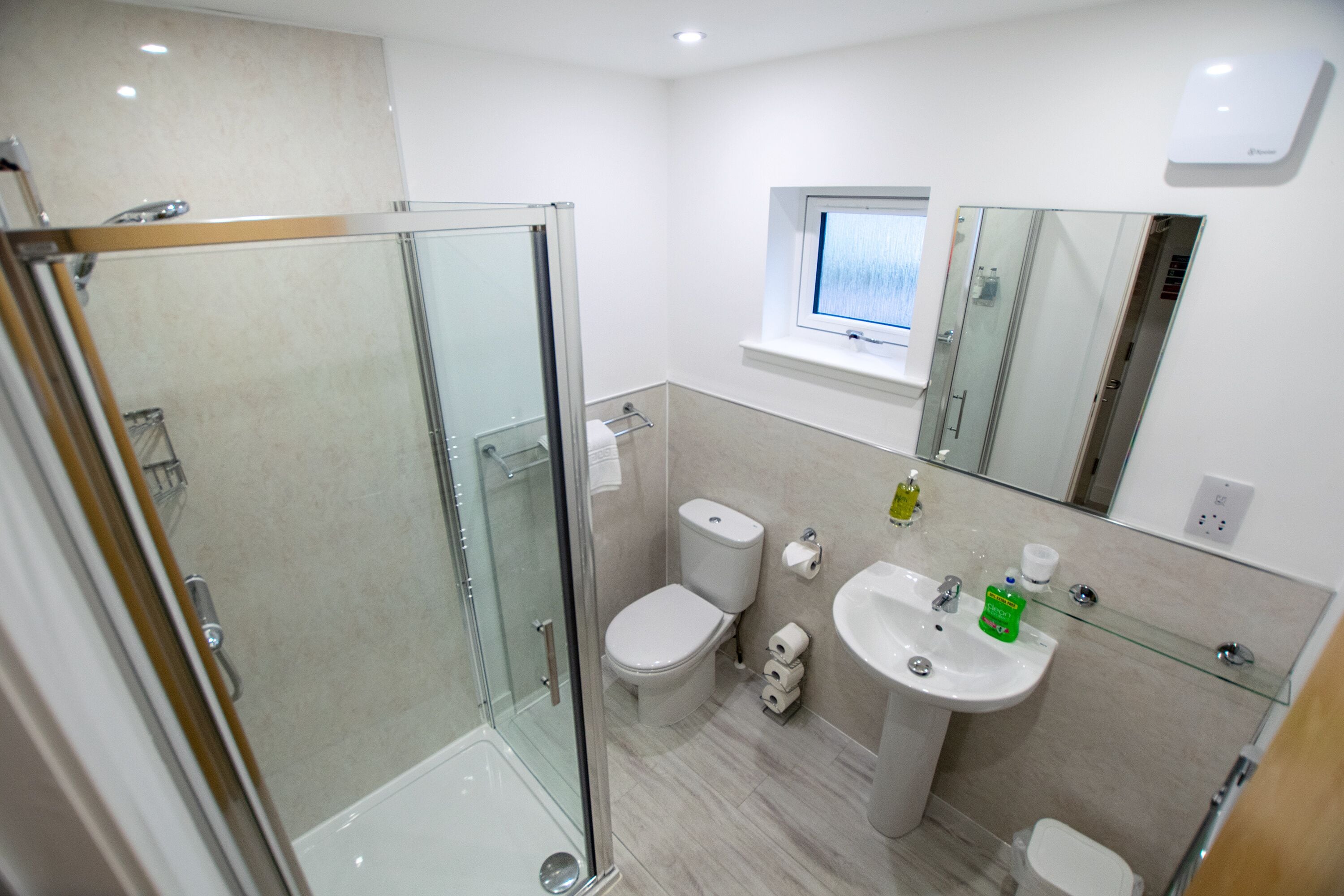 Un baño moderno con ducha de vidrio, inodoro, lavabo y espejo.