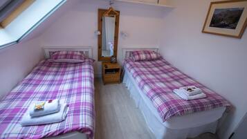 Un dormitorio con dos camas, cada una con cubrecama y almohadas a cuadros. Entre las camas hay una mesita de noche de madera, un espejo sobre la mesita y un cuadro en la pared.