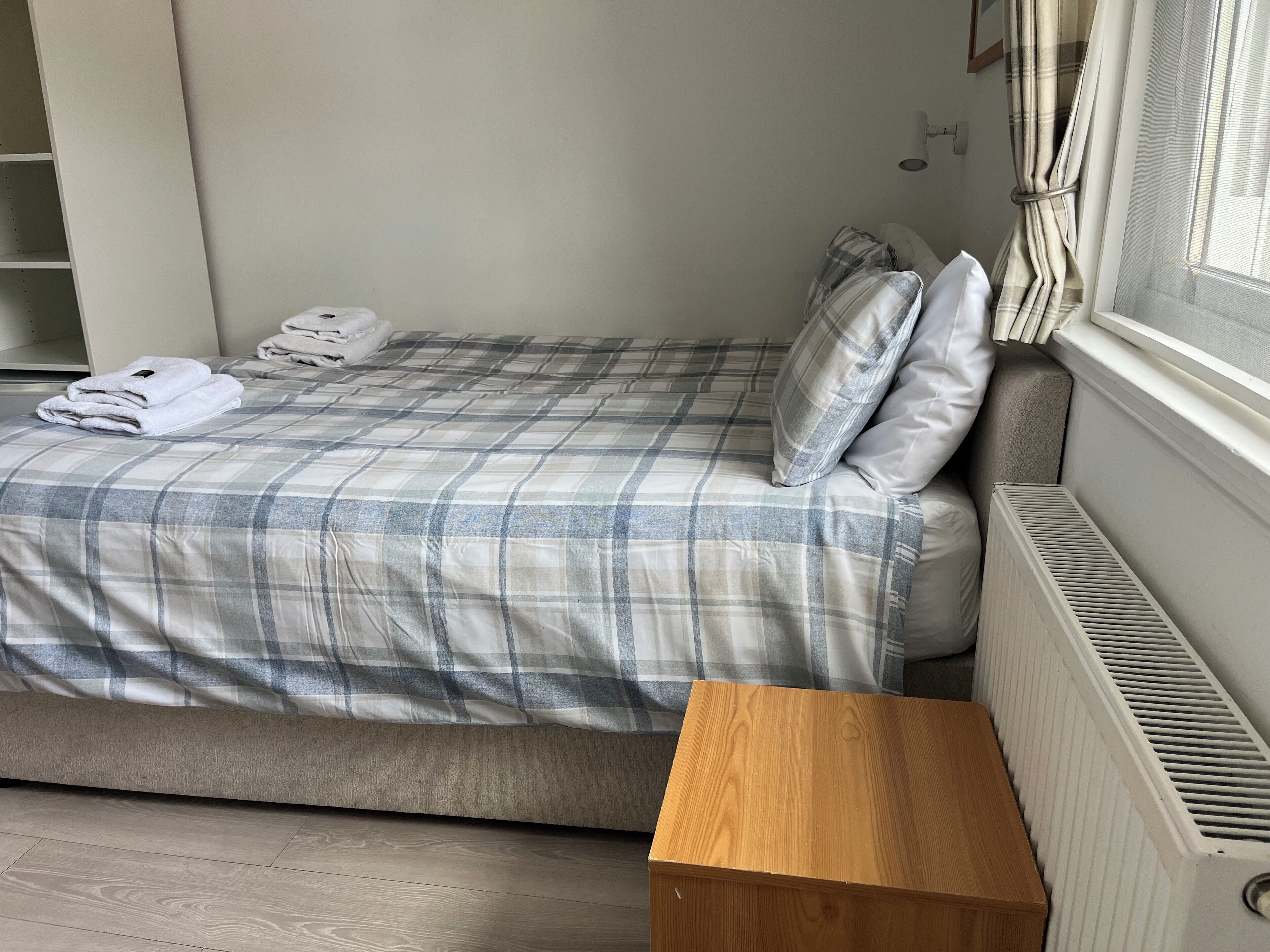 Une chambre à coucher avec un lit, des oreillers, une table de chevet en bois et un radiateur.