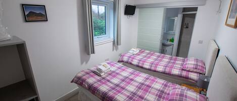 A bedroom with two beds, a window, a mirror, a TV, and a bathroom visible through the mirror.