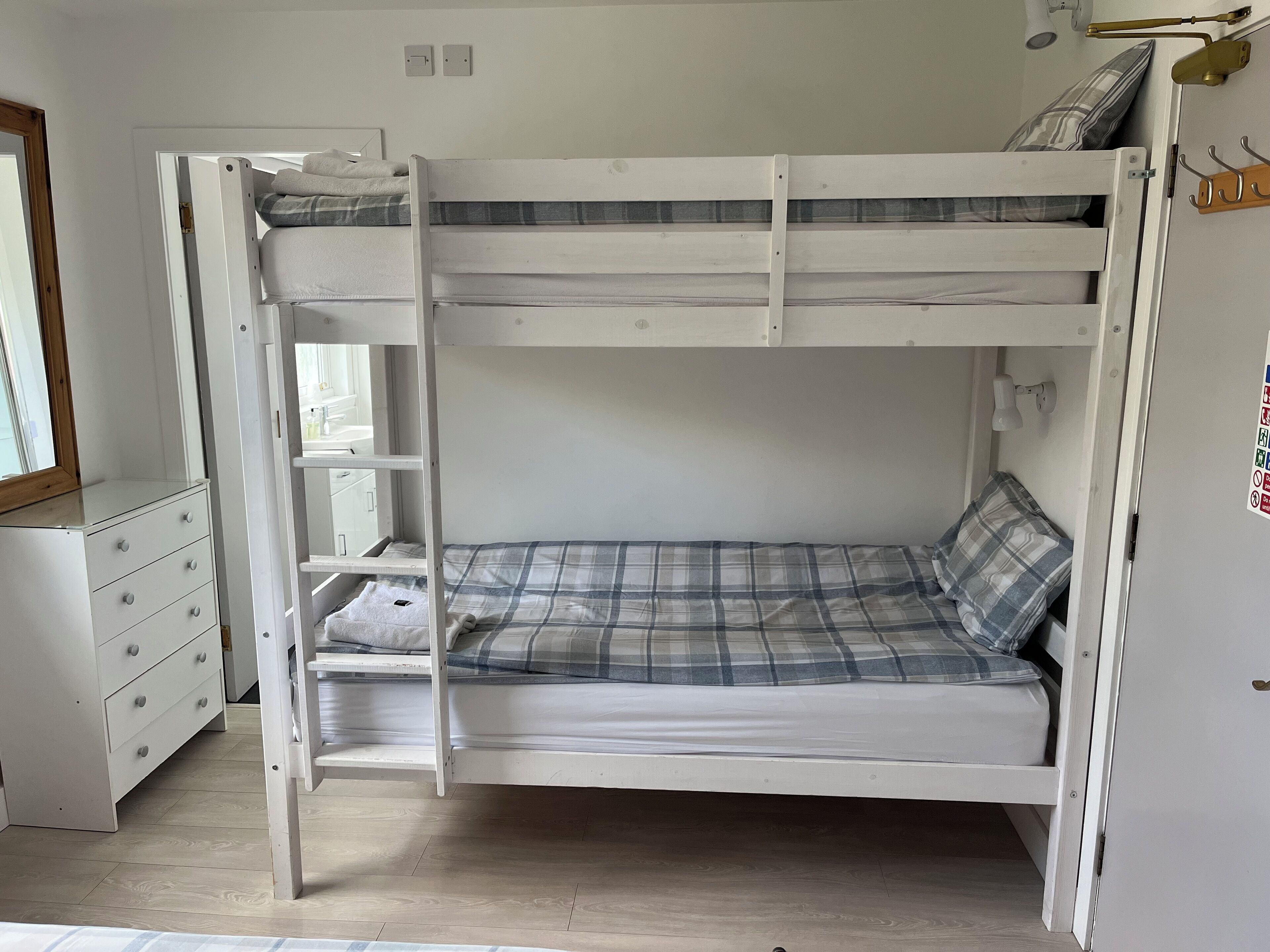 Una cama individual superpuesta con escalera, un aparador con cajones y un espejo.