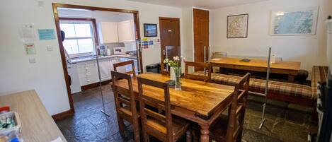 A dining area with a wooden table and chairs, a kitchen in the background, and a map on the wall.