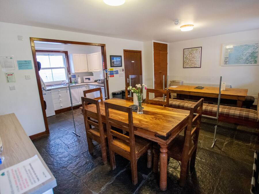 A dining area with a wooden table and chairs, a kitchen in the background, and a map on the wall.