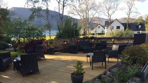 Une terrasse extérieure avec des meubles en osier, une plateforme en bois et une vue sur les montagnes.