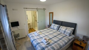 Une chambre à coucher avec un lit, une télévision, une table de chevet et une salle de bain visible à travers une porte ouverte.