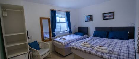 A bedroom with two beds, a chair, a wardrobe, and a window with curtains.