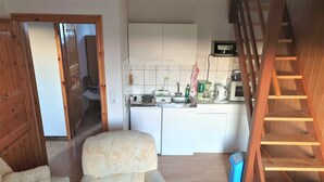 A compact living space with a sofa, a small rug, a kitchen area with appliances, and a wooden staircase.