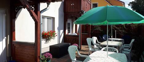 A patio area with a table and chairs under a green umbrella, a wooden fence, and potted plants.