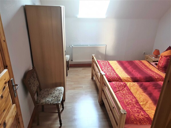 A bedroom with a wooden bed, a chair, a radiator, and a window. - Vacation apartment 2 - Stork view (Dargen)
