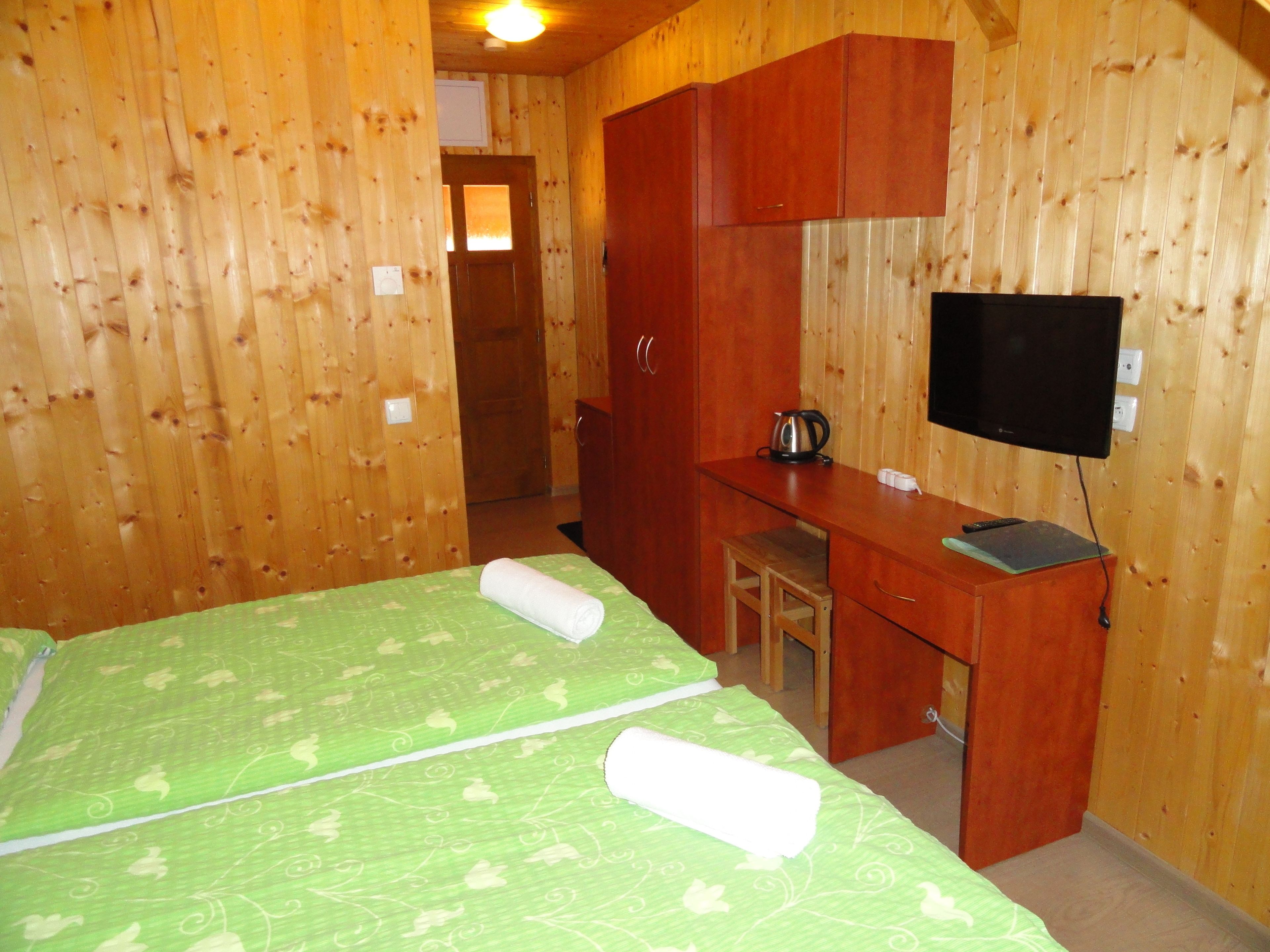 Habitación de madera con dos camas, un escritorio, un televisor y una tetera.