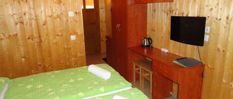 Habitación de madera con dos camas, un escritorio, un televisor y una tetera.