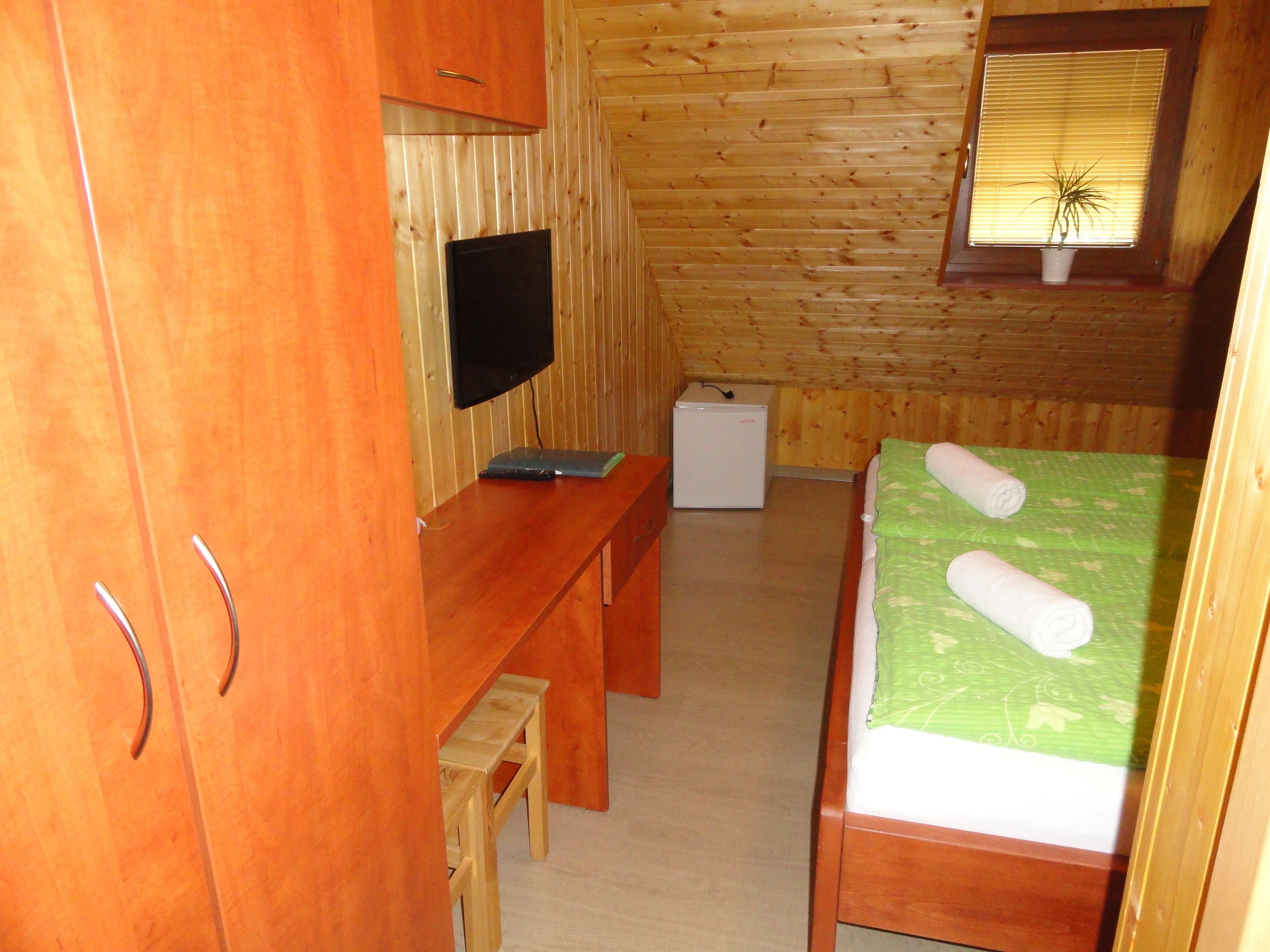 A small, wooden-paneled room with a bed, a desk, a television, and a small refrigerator.