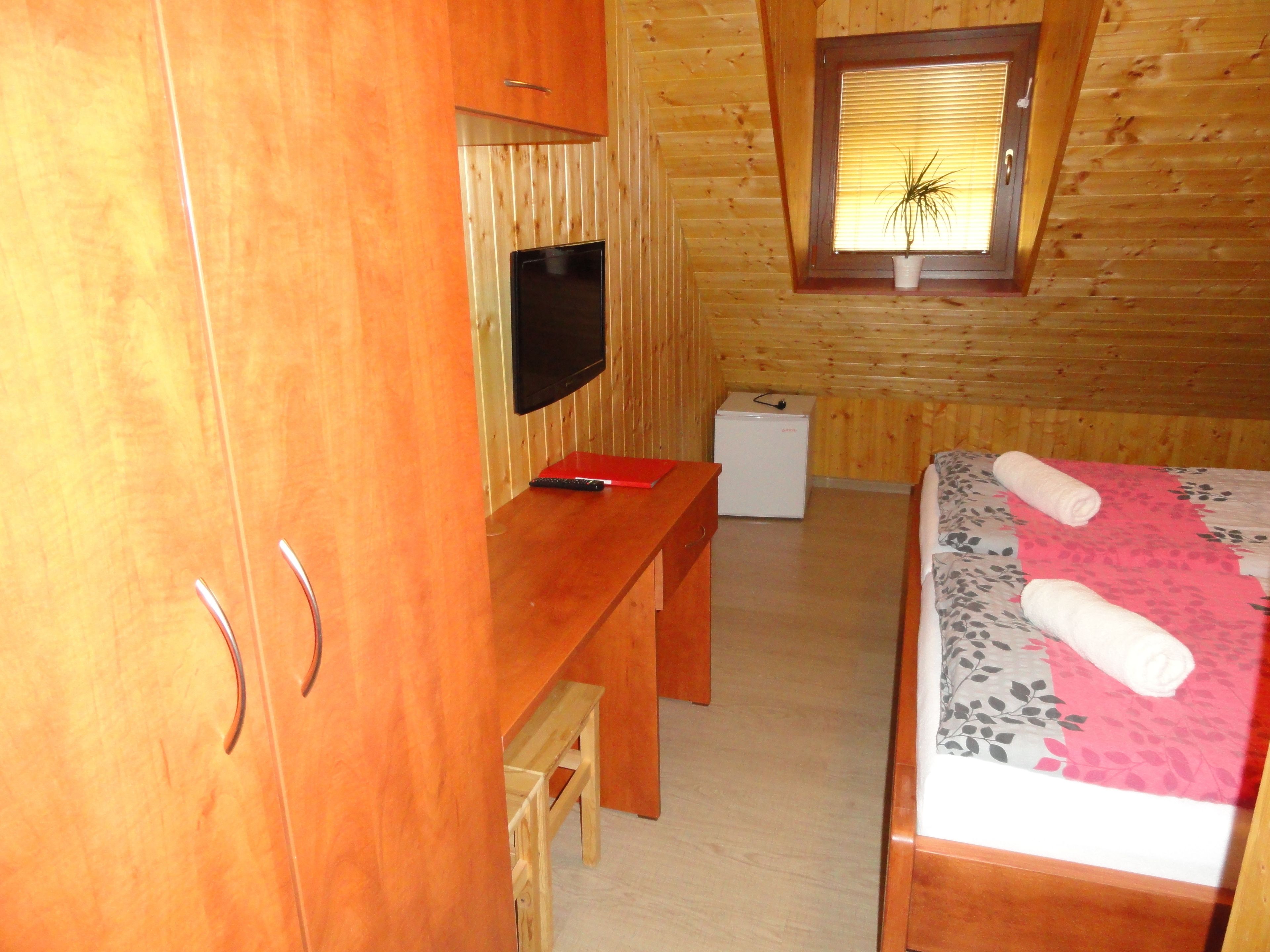 A wooden-paneled room with a bed, a desk, a television, and a small refrigerator.