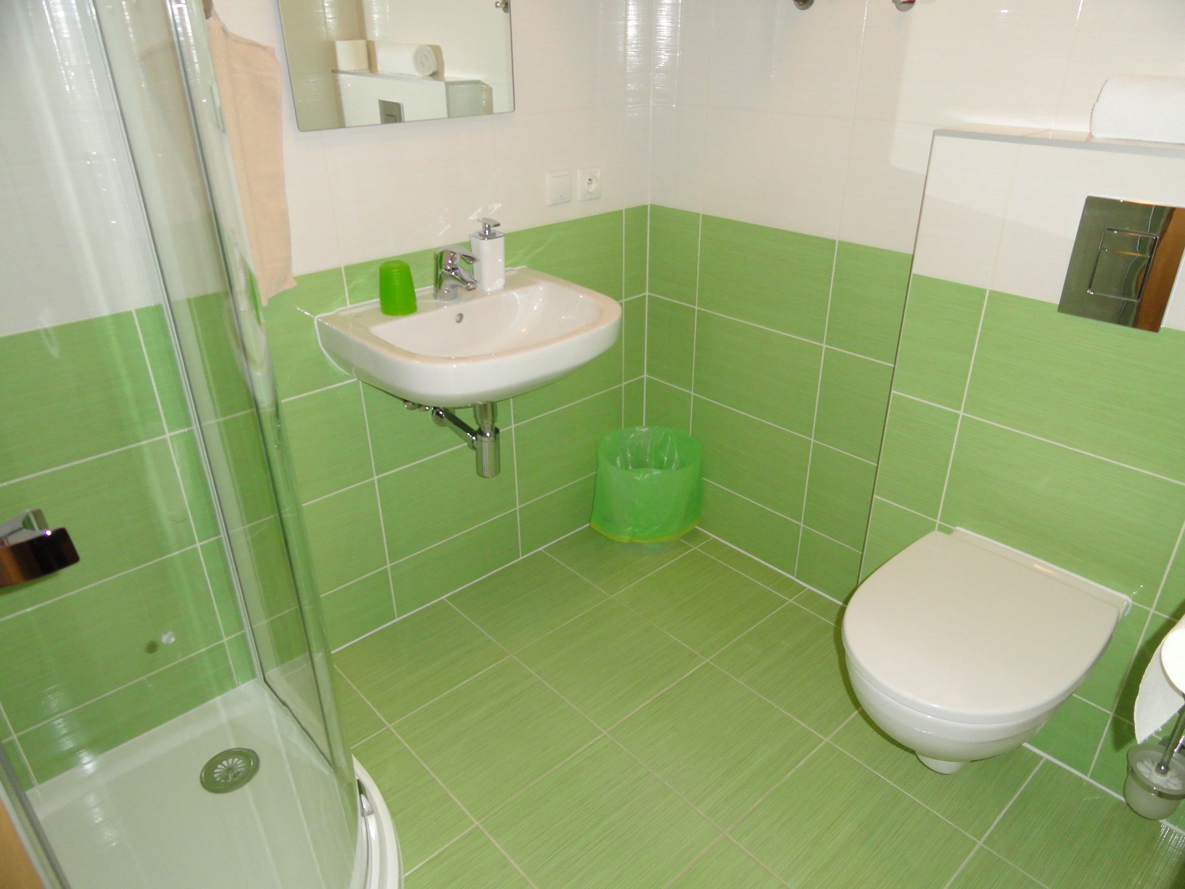 A bathroom with green tiles, a sink, a toilet, and a shower.