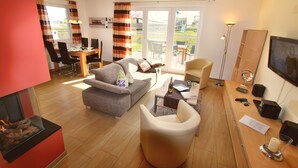 Een moderne woonkamer met een open haard, een bank, een eettafel met stoelen, en een balkon met tuinmeubilair.