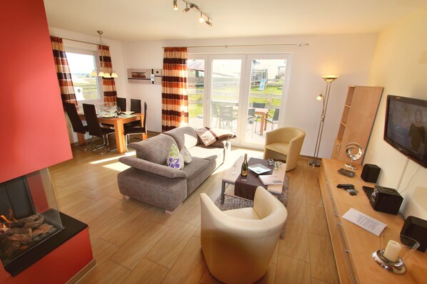 Ein modernes Wohnzimmer mit Kamin, einer Couch, einem Esstisch mit Stühlen und einem Balkon mit Gartenmöbeln.