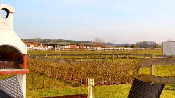Een terras met een barbecue, uitzicht op een wijngaard en een complex van gebouwen in de verte.