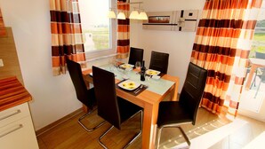 Een eethoek met een tafel voor vier personen, stoelen, een raam met gordijnen en een plafondventilator.