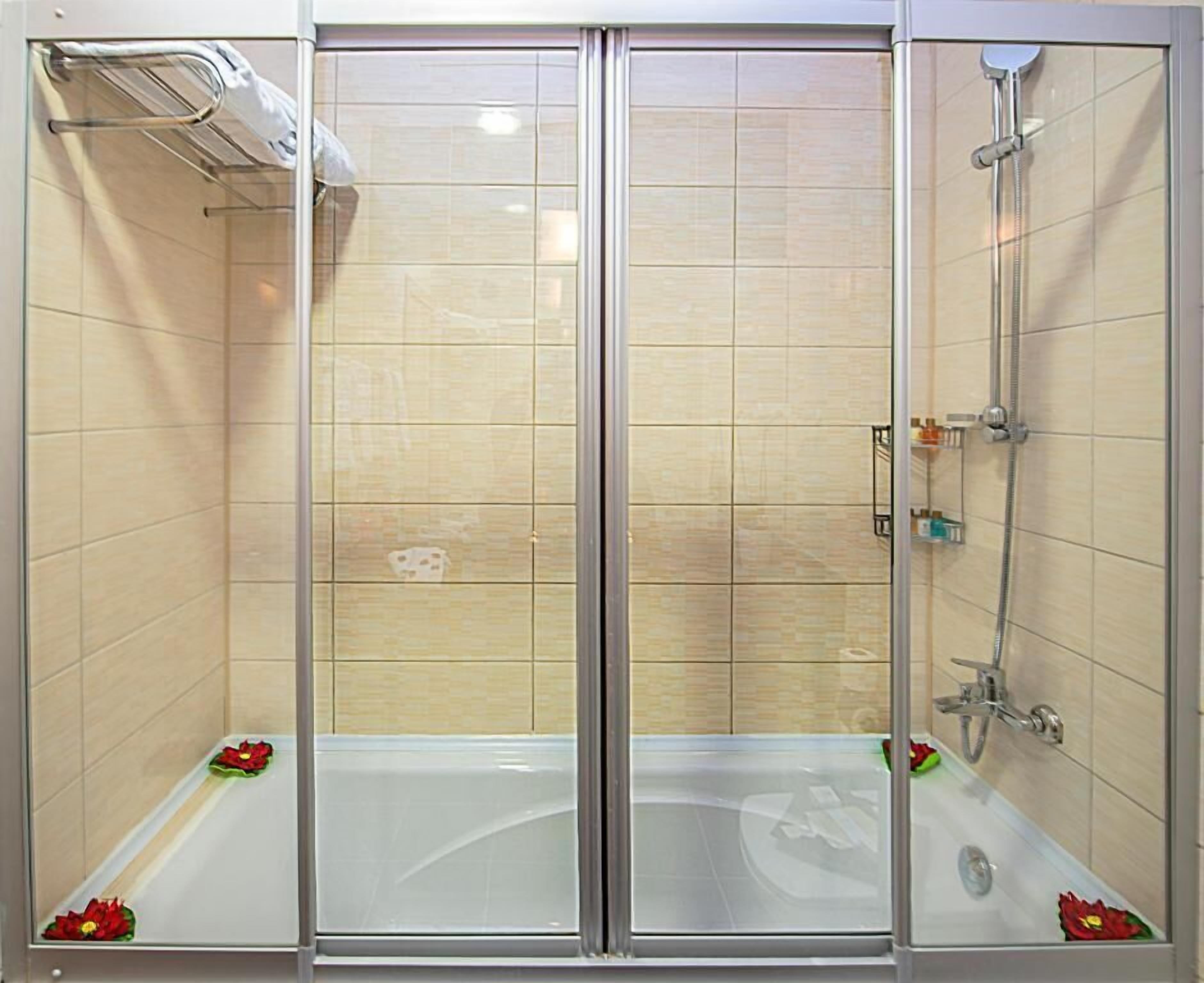 Zona de ducha con mampara de vidrio, bañera, paredes con azulejos y ducha.