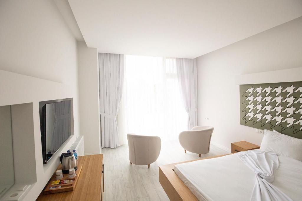 Habitación de hotel con cama, televisión, mesita de madera con bandeja, dos sillas y vistas al exterior.
