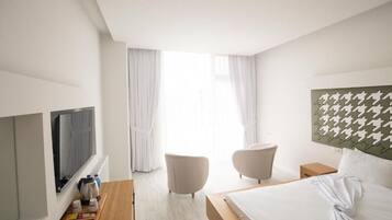 Habitación de hotel con cama, televisión, mesita de madera con bandeja, dos sillas y vistas al exterior.
