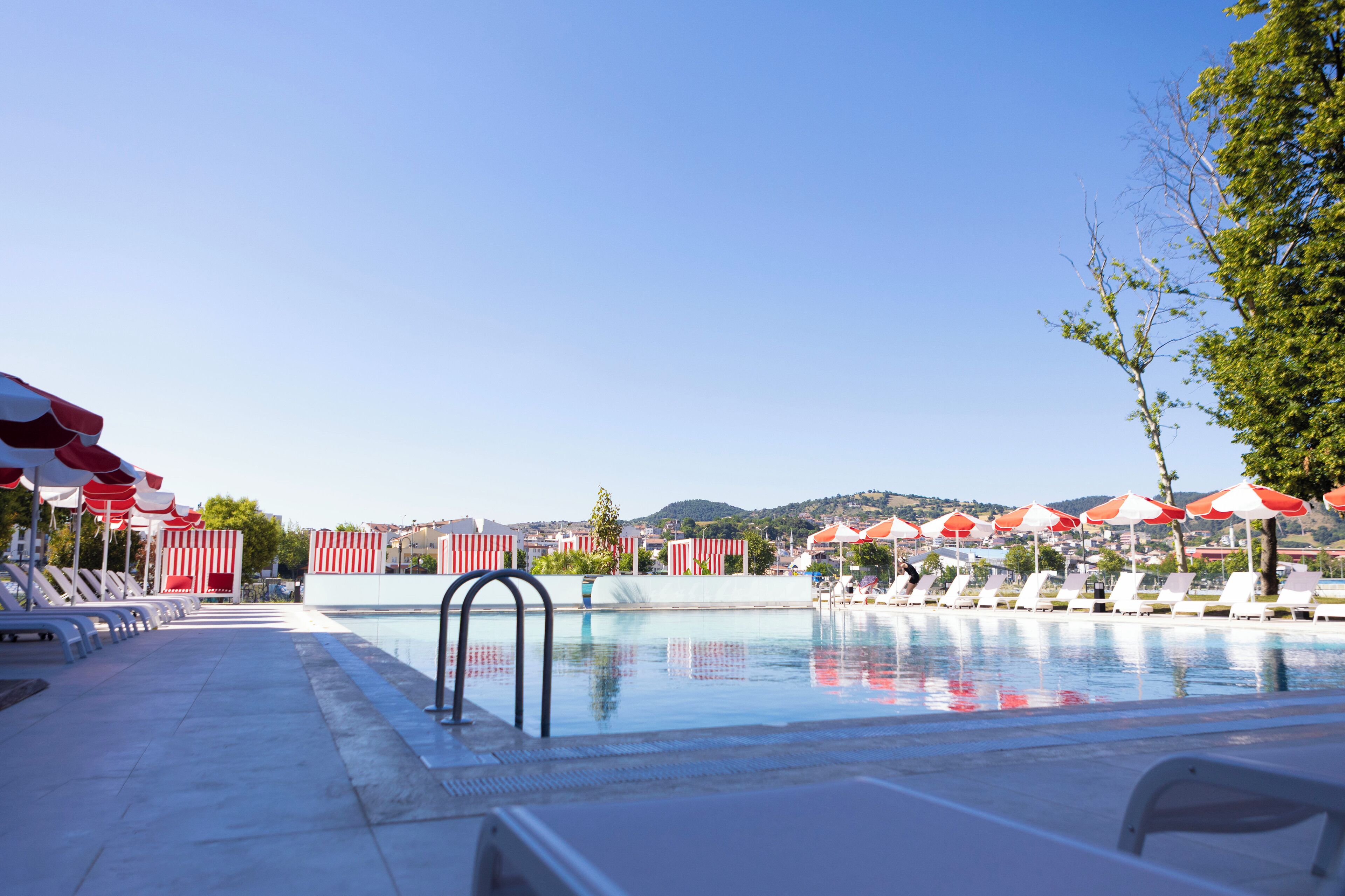 Piscina con barriere a righe rosse e bianche, sedie a sdraio e ombrelloni.