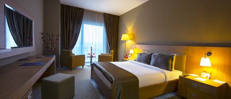 A hotel room with a bed, bedside table, lamp, desk, chair, and a small table with a vase.