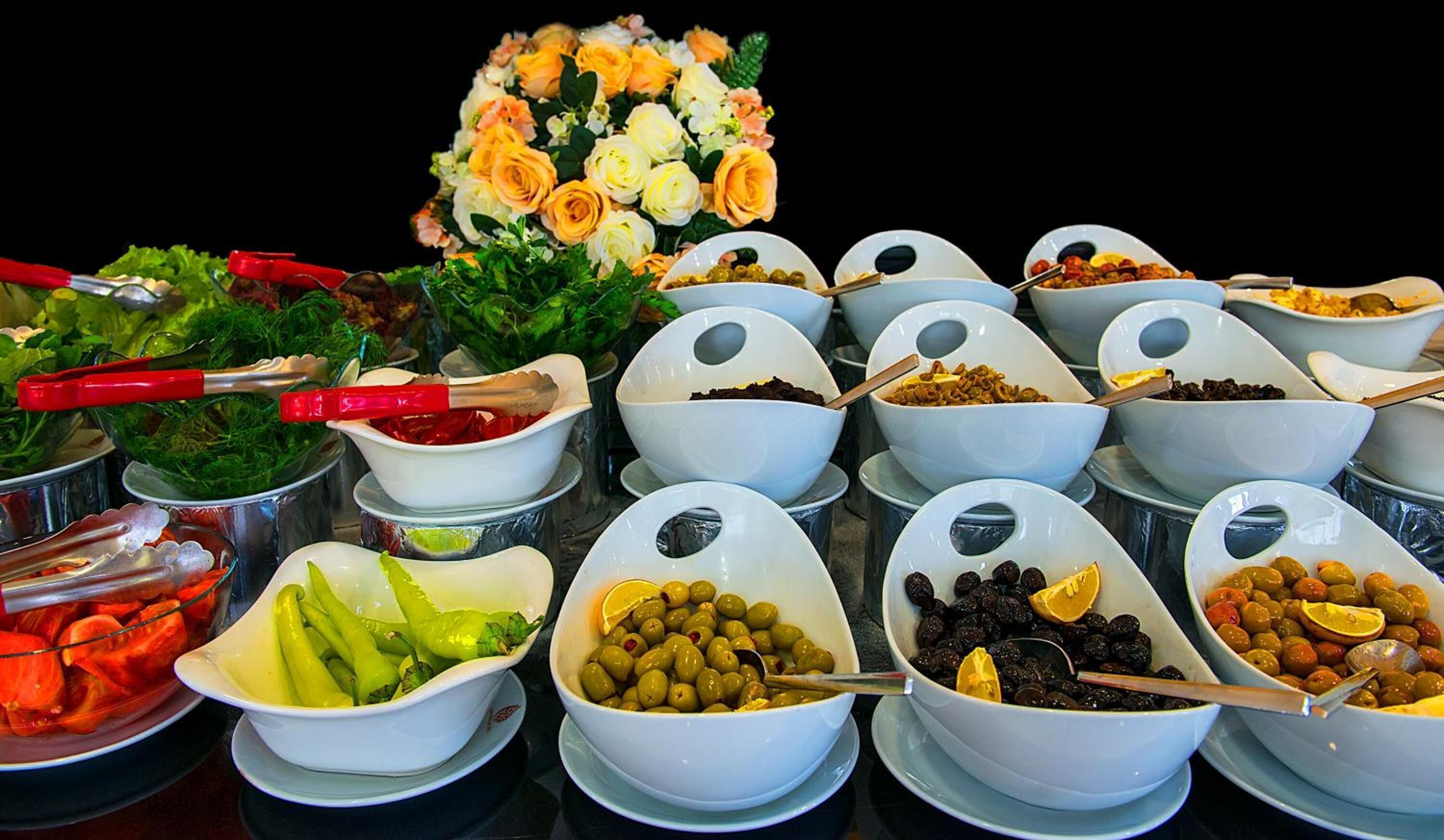 Un buffet con diversi piatti, tra cui olive, sottaceti e un centrotavola floreale.
