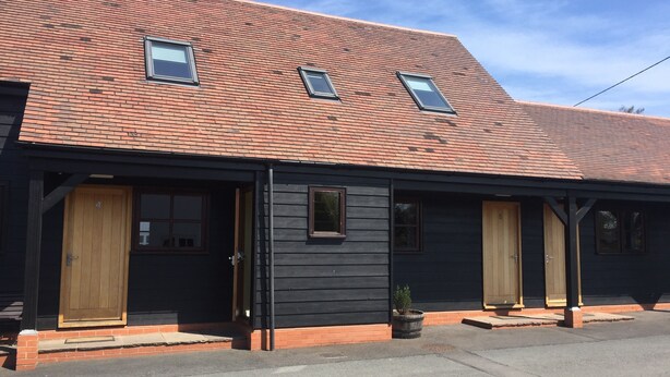 A two-story building with a red-tiled roof, black siding, and two wooden doors. - The Corners Inn (Leominster)