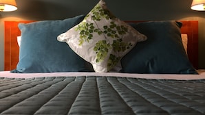 A bed with a quilted cover and two pillows, one with a floral pattern and the other solid blue. - The Corners Inn (Leominster)