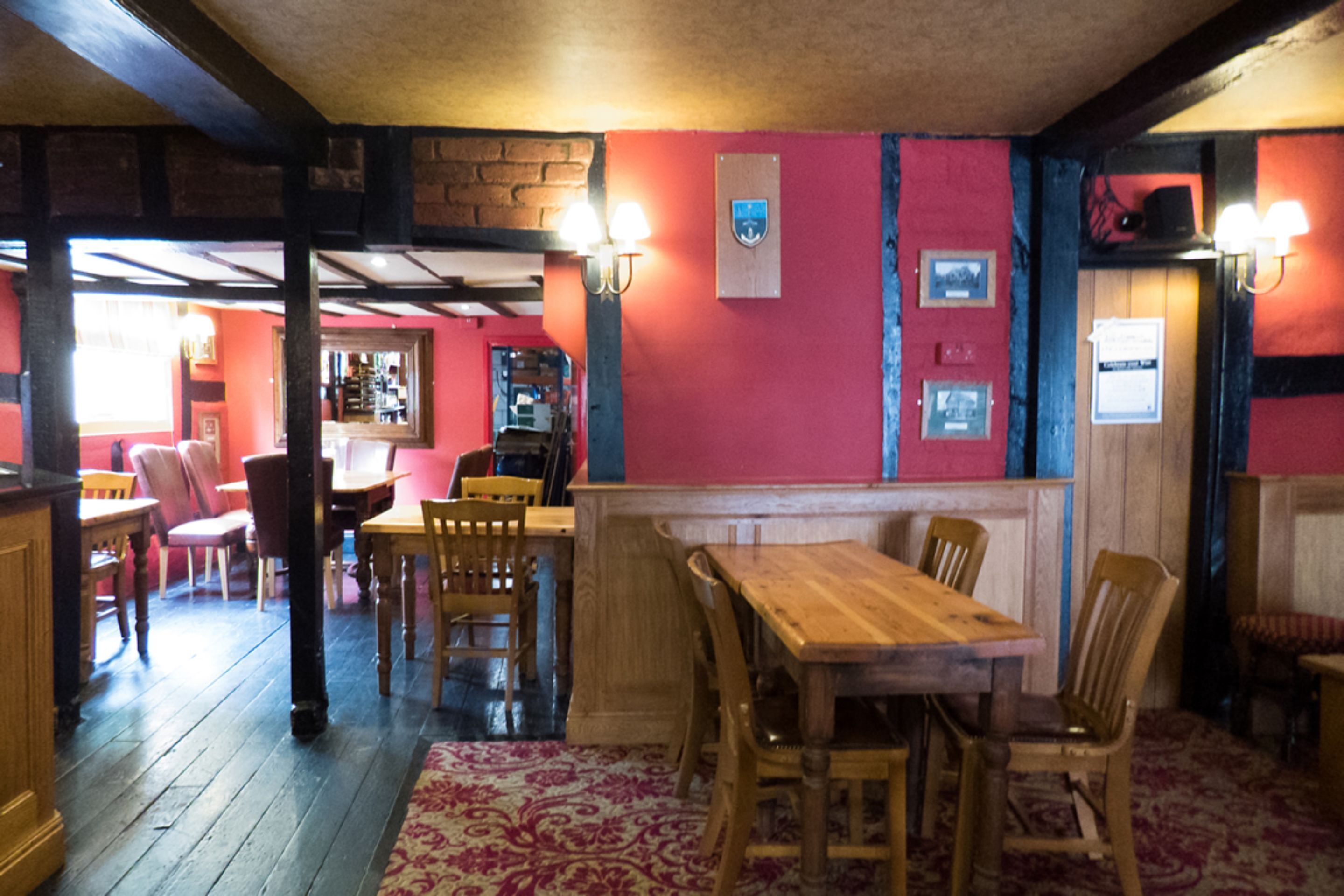 Een restaurantinterieur met houten tafels en stoelen, een rode muur met ingelijste foto's en een bakstenen muur op de achtergrond.