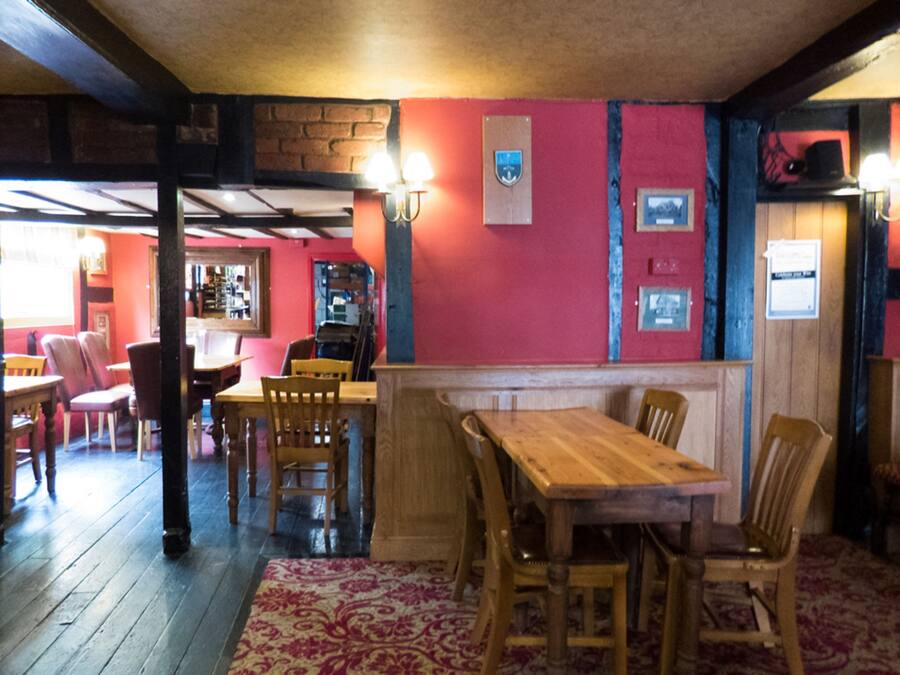 A restaurant interior with wooden tables and chairs, a red wall with framed pictures, and a brick wall in the background.