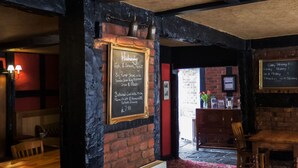 A restaurant interior with a chalkboard menu, wooden furniture, and brick walls. - The Corners Inn (Leominster)