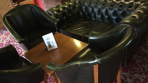 A black leather sofa and two matching armchairs with a wooden table in between, placed on a patterned carpet. - The Corners Inn (Leominster)