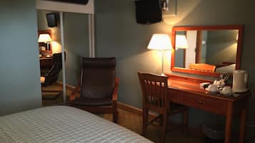 A hotel room with a bed, a desk, a chair, a lamp, a mirror, and a television on the wall.