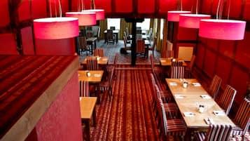 Un comedor con paredes rojas, sillas a rayas y una alfombra estampada. Las mesas están dispuestas con manteles blancos y centros de mesa.