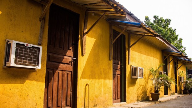 A yellow building with wooden doors and windows, an air conditioning unit, and potted plants. - Castle City Resort & Suites (Lekki)