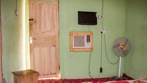 A room with a wooden door, a wall-mounted air conditioner, a standing fan, and a small wooden stool. - Castle City Resort & Suites (Lekki)