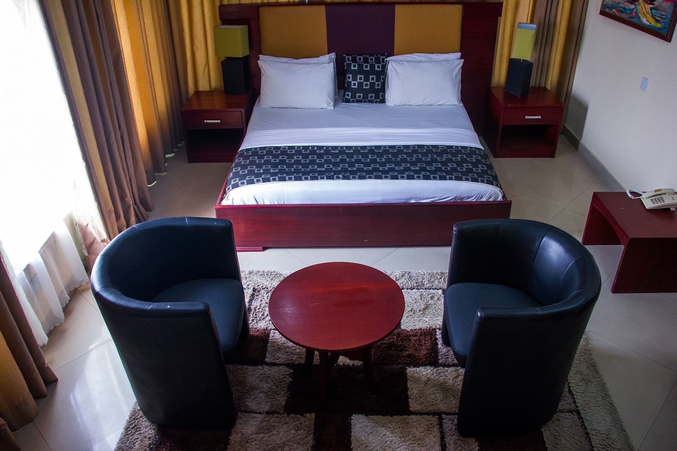 A hotel room with a bed, two armchairs, a small table, and a nightstand with a phone.