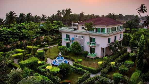 A two-story building with a garden in front, surrounded by palm trees.