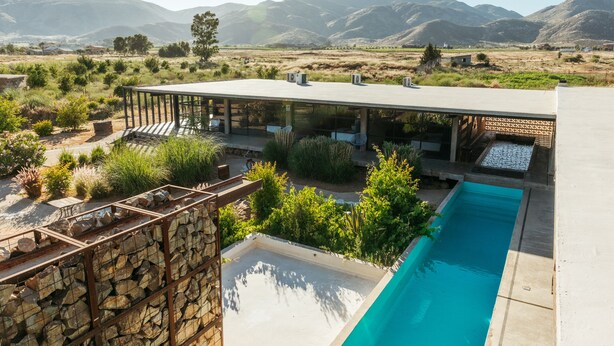 A modern house with a pool, surrounded by mountains and greenery.