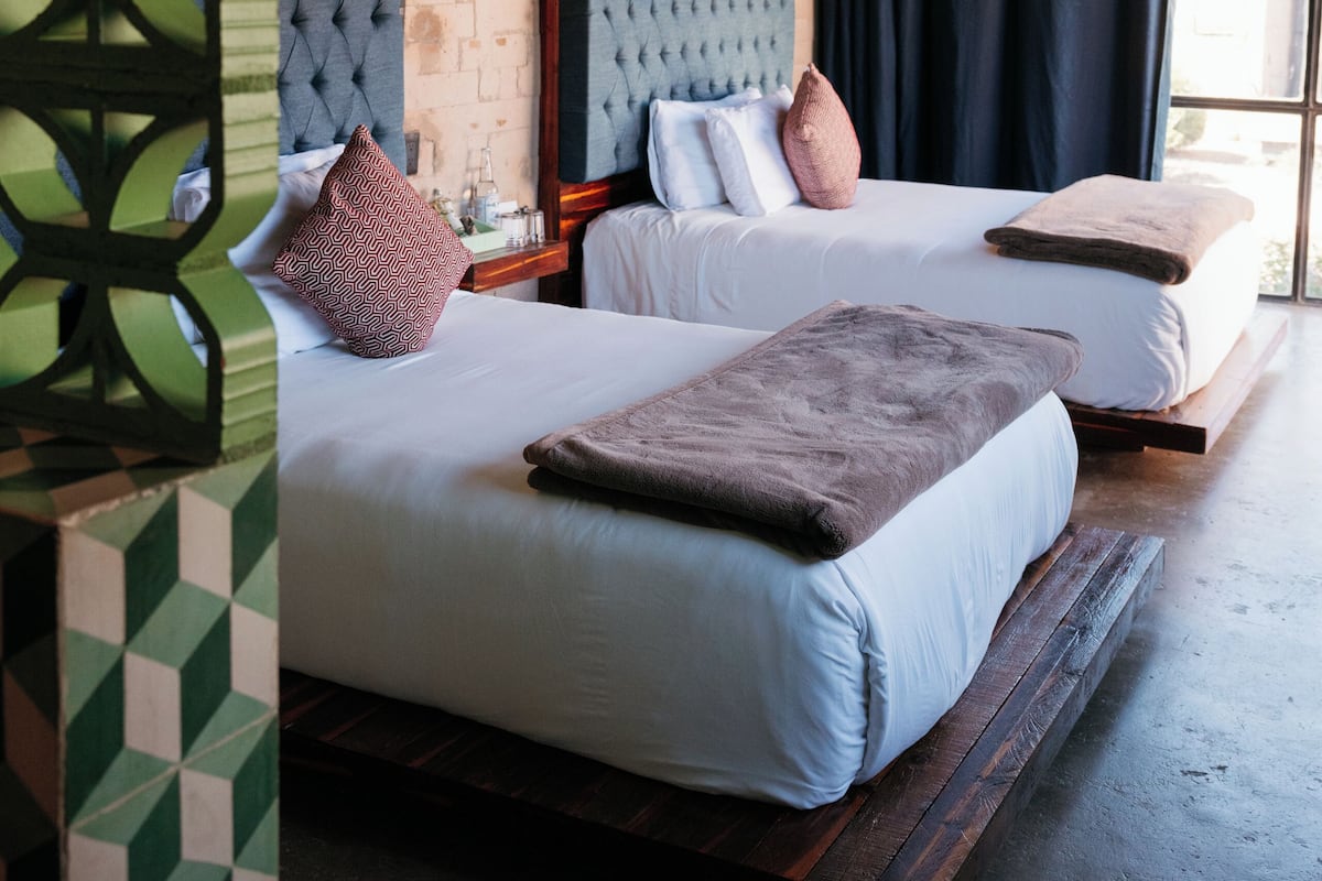 A modern hotel room with two beds, a brick wall, and a large window with curtains.