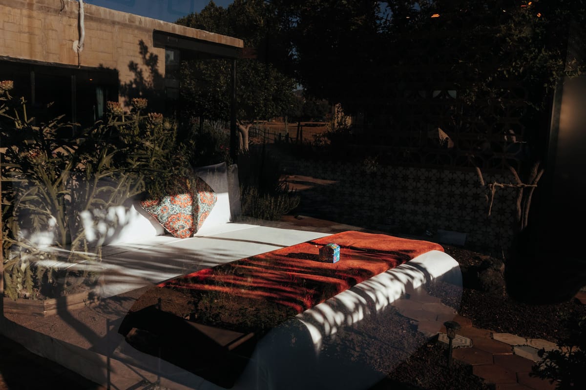 A modern outdoor seating area with a white sofa, a large planter, and a red rug.