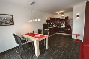A modern kitchen with dark tiles, a dining area with a red table, and a red sofa.