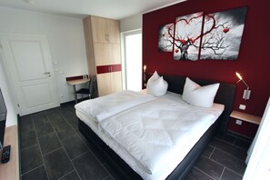 A modern bedroom with a large bed, a wardrobe, a desk, and a wall-mounted artwork.