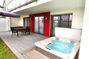 A patio with a hot tub, a table with chairs, and a red wall.