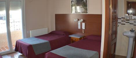 Habitación de hotel con dos camas, una mesita de noche pequeña, teléfono, equipo de aire acondicionado y baño con lavamanos.