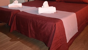 A hotel room with two beds, each with a red bedspread and white towels. There is a wooden headboard, a painting of a building on the wall, and a door with a glass panel. - Hostal Alamare (Seville)