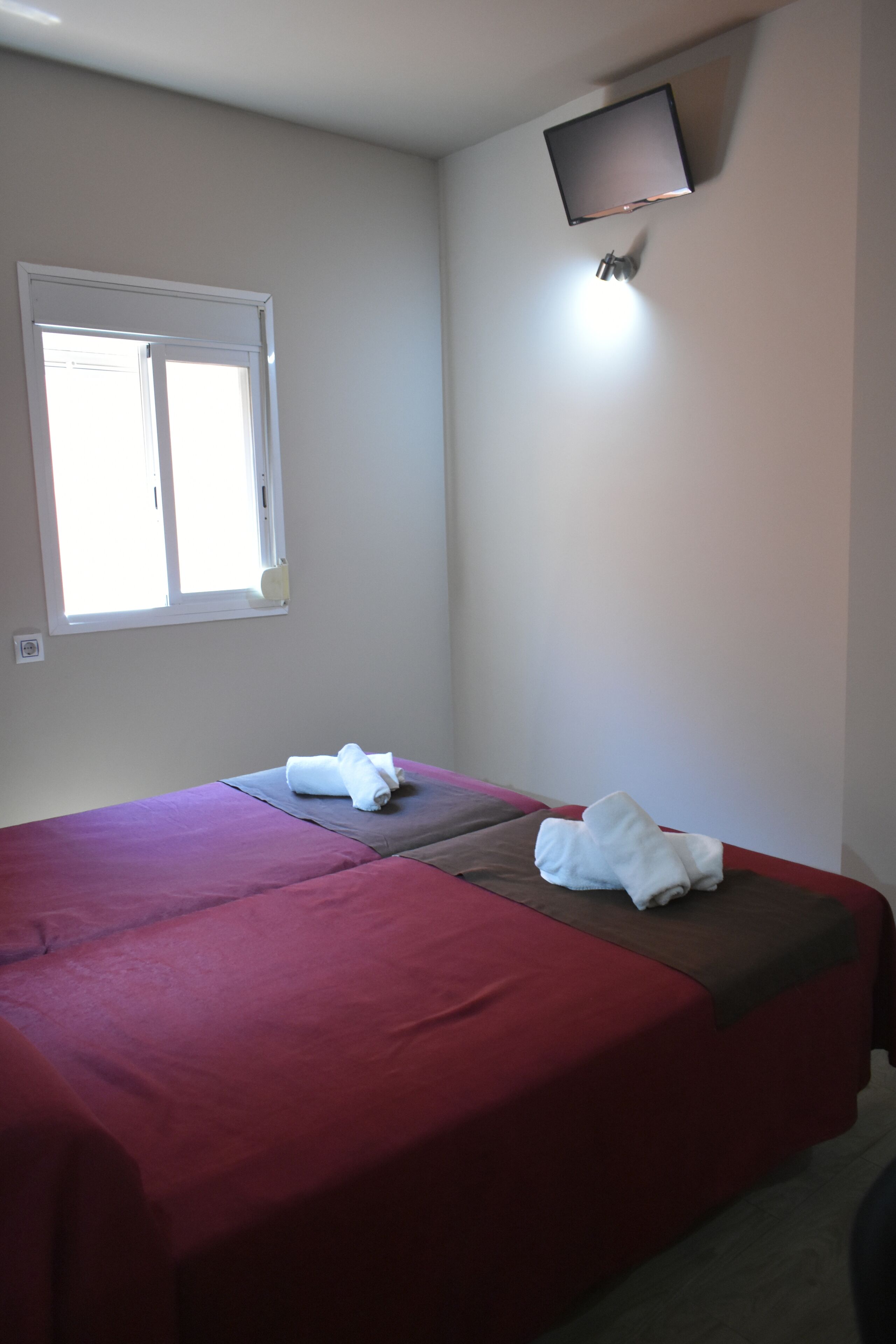 Habitación de hotel con dos camas, un televisor montado en la pared y una ventana con persianas.